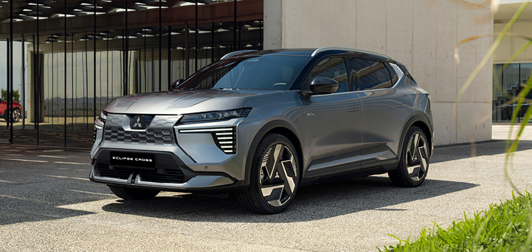 Grauer Mitsubishi Eclipse Cross im Dreiviertelprofil, geparkt vor einem modernen Gebäude mit Glasfassade und Betonwand bei Tageslicht.